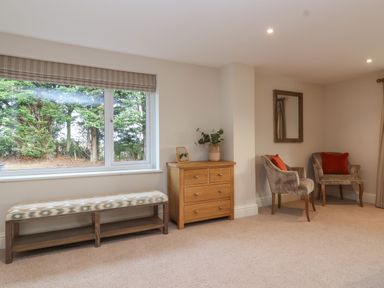 A room with a window bench a wooden chest of drawers and two armchairs with orange cushions at Blossom Hill near Witney