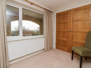 A room with a window showing an outdoor stone arch with beige curtains a radiator wooden double closet doors and a green chair at Blossom Hill near Witney