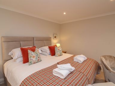 A bedroom with a large bed featuring floral and orange pillows and folded towels on a patterned bedspread at Blossom Hill near Witney