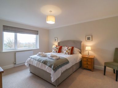 A bedroom with a double bed two bedside tables with lamps a window and an upholstered chair at Blossom Hill near Witney