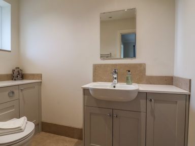 A bathroom with a sink, mirror, soap dispenser, toilet, and cabinets at Blossom Hill near Witney