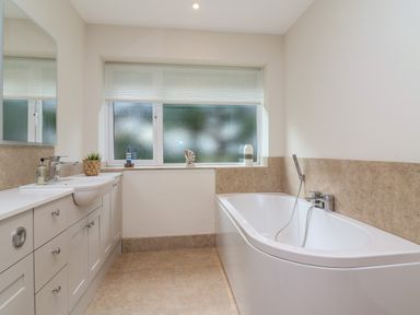 A bathroom with a bathtub and a sink with cabinets below a frosted window at Blossom Hill near Witney