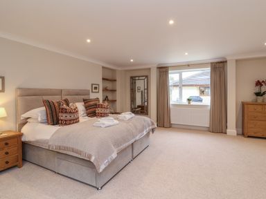 A bedroom with a large bed pillows bedside table lamps mirror window and chest of drawers at Blossom Hill near Witney