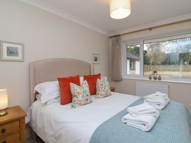 A bedroom with a bed with colorful pillows bedside tables a window and folded towels at Blossom Hill near Witney