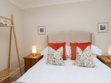 A bedroom with a bed with floral and red pillows and wooden bedside tables with lamps at Blossom Hill near Witney