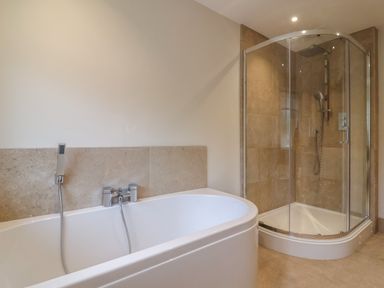 A bathroom with a white bathtub and a glass enclosed shower at Blossom Hill near Witney