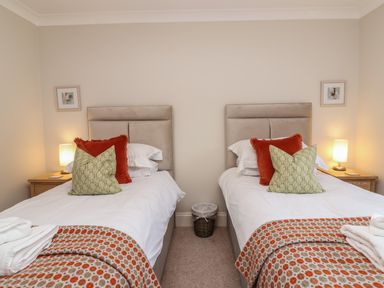A bedroom with two single beds with patterned blankets and cushions with bedside tables and lamps at Blossom Hill near Witney