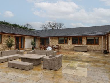 An outdoor patio area with wicker seating and tables in front of a stone building at Blossom Hill near Witney