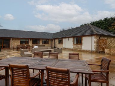 An outdoor patio with multiple wooden tables and chairs in front of a single-story stone building at Blossom Hill near Witney