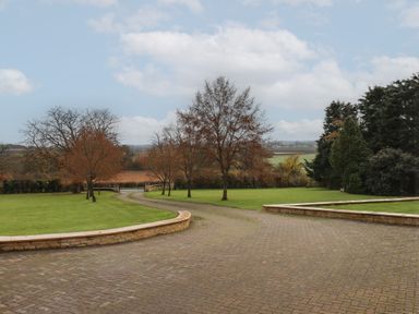 A paved driveway with low brick walls bordered by grass and trees at Blossom Hill near Witney