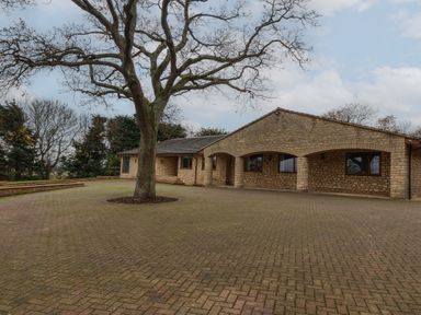 A brick house with arches and a large tree in a paved courtyard at Blossom Hill near Witney