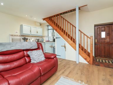 A sitting area with a red sofa next to a kitchen and wooden staircase at Badgers Sett in Stibb near Kilkhampton