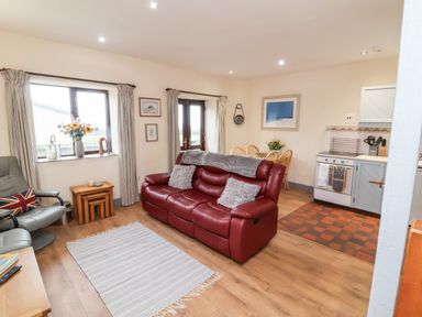 A living room and kitchen area with a red leather sofa gray chair wooden dining table and kitchen appliances at Badgers Sett in Stibb near Kilkhampton