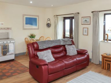 A living room with a red sofa and dining table next to kitchen appliances at Badgers Sett in Stibb near Kilkhampton