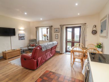 A living room with a red sofa a grey chair and a wooden dining table with chairs at Badgers Sett in Stibb near Kilkhampton
