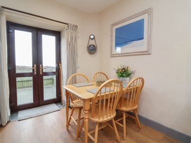 A wooden dining table with four chairs near glass doors leading outside at Badgers Sett in Stibb near Kilkhampton