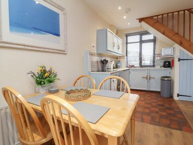 A kitchen and dining area with a wooden table and chairs a floral arrangement a window with blinds and light blue cabinets at Badgers Sett in Stibb near Kilkhampton