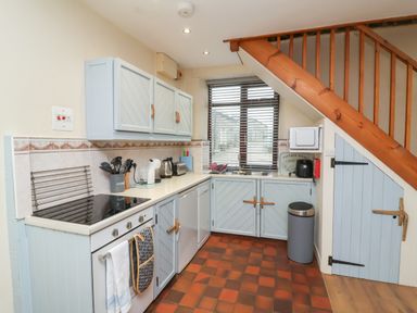A kitchen with light blue cabinets under and over the counter and a wooden staircase at Badgers Sett in Stibb near Kilkhampton