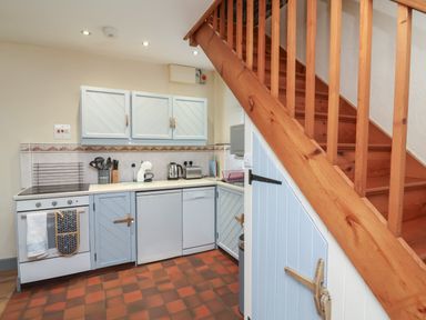 A kitchen with blue cabinets appliances and wooden stairs at Badgers Sett in Stibb near Kilkhampton
