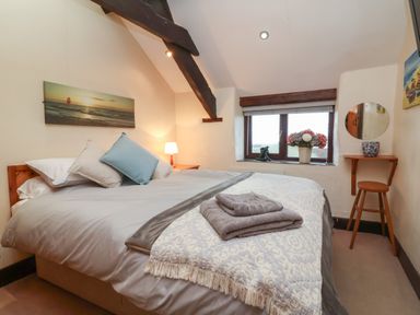 A bedroom with a double bed pillows bedside table lamp window flowers and a stool at Badgers Sett in Stibb near Kilkhampton