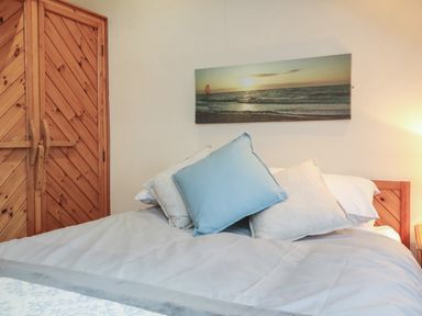 A bedroom with a bed with pillows and a wooden wardrobe and a seascape picture on the wall at Badgers Sett in Stibb near Kilkhampton