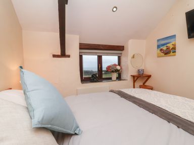A bedroom with a bed and pillows near a window with flowers at Badgers Sett in Stibb near Kilkhampton