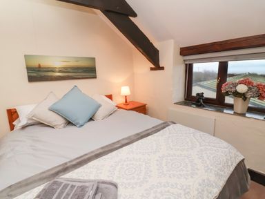 A bedroom with a double bed nightstand and window with flowers at Badgers Sett in Stibb near Kilkhampton
