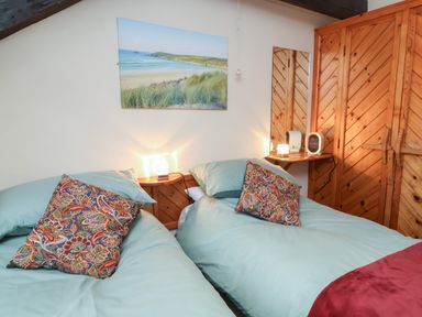 A bedroom with two single beds with blue bedding and patterned cushions a wooden wardrobe and a beach landscape picture on the wall at Badgers Sett in Stibb near Kilkhampton