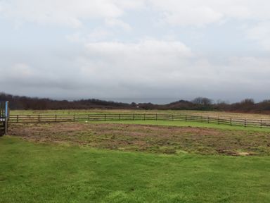 A fenced paddock with green grass and brown patches under a cloudy sky at Badgers Sett in Stibb near Kilkhampton