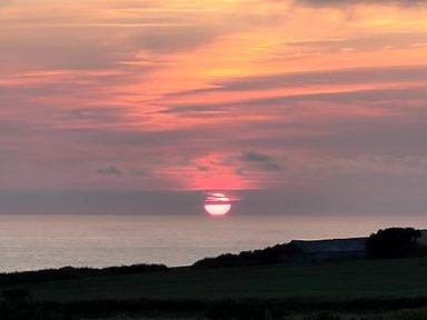 A sunset over the ocean with a silhouette of land at Badgers Sett Stibb near Kilkhampton