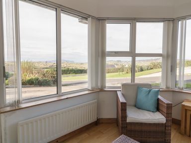 A corner room with large windows wicker armchair with cushions and wooden side table at Horn Head View in Carrigart County Donegal