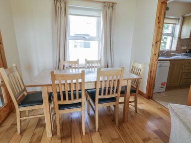 A dining room with a wooden table and six chairs next to a window and an open doorway to a kitchen at Horn Head View in Carrigart County Donegal