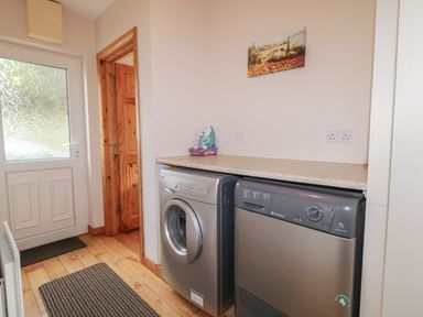A laundry room with washing machine and dryer under a countertop next to a door at Horn Head View in Carrigart County Donegal
