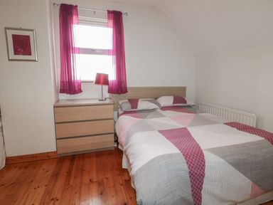A bedroom with a double bed a wooden chest of drawers and a window with red curtains at Horn Head View in Carrigart County Donegal