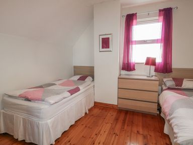 A bedroom with two single beds a wooden dresser and a window with purple curtains at Horn Head View in Carrigart County Donegal