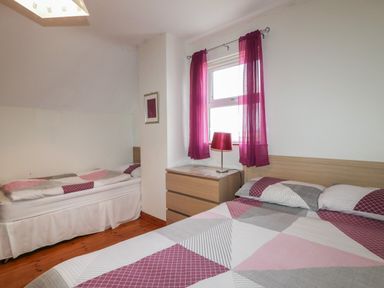 A bedroom with two beds a wooden dresser a window with purple curtains and a red lamp at Horn Head View in Carrigart County Donegal
