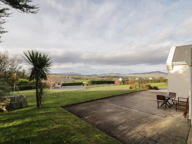 A backyard with patio furniture next to a house and a lawn with trees and houses in the distance at Horn Head View in Carrigart County Donegal