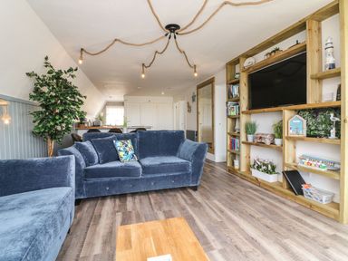A living room with blue sofas wooden shelves with plants and decor and rope lighting at La Bella Vista in Kilkhampton