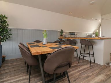 A dining area with a wooden table and six chairs next to a kitchen counter with bar stools at La Bella Vista in Kilkhampton