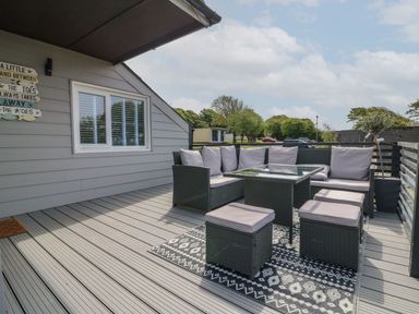 An outdoor deck with a seating area including a corner sofa table and four cushioned stools at La Bella Vista in Kilkhampton