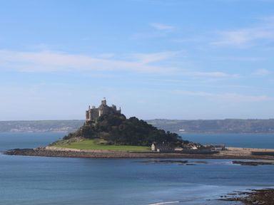 An island with a castle and buildings surrounded by water with distant land in the background at The Packing House in Rosudgeon
