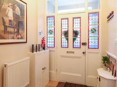 An entryway with stained glass front door a small cabinet a radiator a framed painting a plant on a corner shelf and a fire extinguisher at Grosvenor House in Kirkley Rise