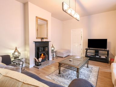A living room with a fireplace a wall mirror a television on a stand a glass coffee table two sofas and two side tables Grosvenor House Kirkley Rise