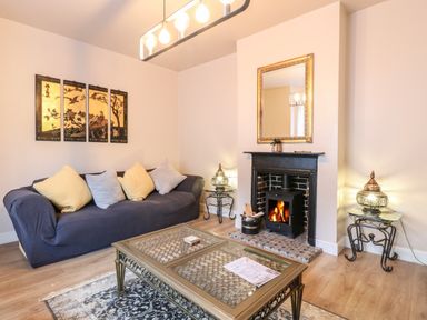 A living room with a blue sofa and cushions a coffee table a fireplace with a mirror above and decorative lamps on side tables at Grosvenor House in Kirkley Rise