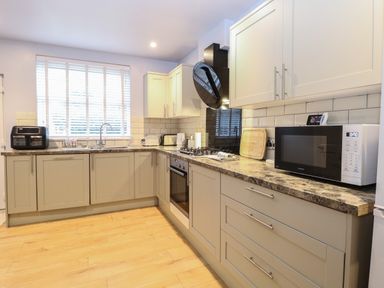 A kitchen with beige cabinets a microwave an oven a gas stove and a window with blinds at Grosvenor House in Kirkley Rise