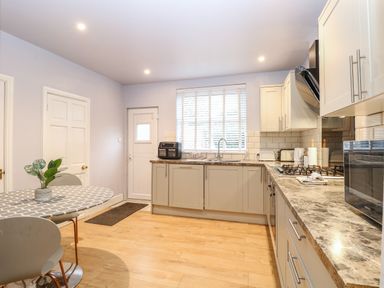 A kitchen with cabinets a countertop a sink a gas stove a microwave a dining table with chairs and a plant Grosvenor House Kirkley Rise