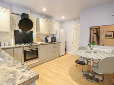 A kitchen with beige cabinets a stove microwave and refrigerator and a round dining table with chairs at Grosvenor House in Kirkley Rise