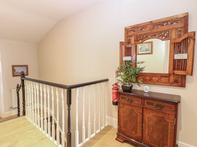 A staircase landing with a wooden cabinet a decorative mirror and a plant at Grosvenor House in Kirkley Rise