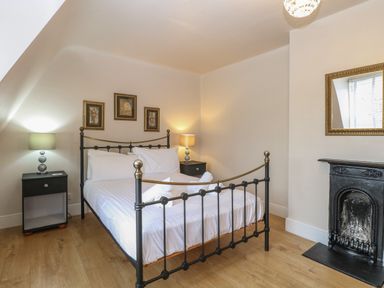 A bedroom with a wrought iron bed two bedside tables with lamps a fireplace and framed pictures on the wall at Grosvenor House in Kirkley Rise
