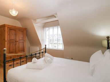 A bedroom with a bed with white linens and rolled towels near a window and a wooden wardrobe at Grosvenor House in Kirkley Rise